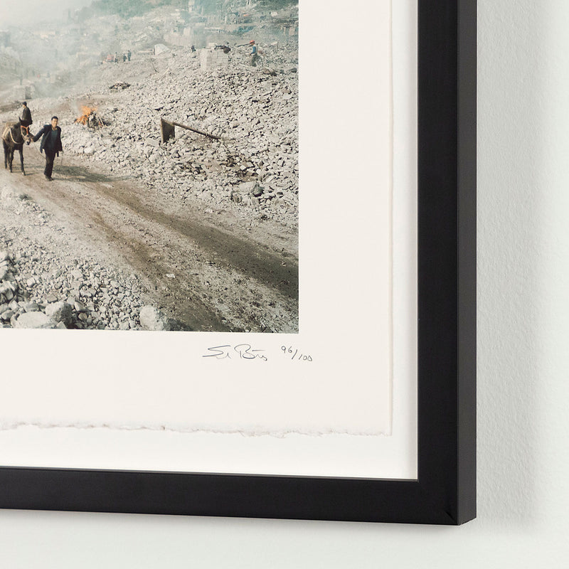 Shot in 2002, Canadian photographer Edward Burtynsky, captures "Feng Jie #5". Depicting a demolished landscape, the photograph is marked by piles of rubble and a dusty haze that obscures the background. Centered in the middle of the work is a man leading his donkey down a dirt road amidst the destruction.