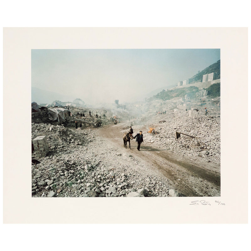 Shot in 2002, Canadian photographer Edward Burtynsky, captures "Feng Jie #5". Depicting a demolished landscape, the photograph is marked by piles of rubble and a dusty haze that obscures the background. Centered in the middle of the work is a man leading his donkey down a dirt road amidst the destruction.