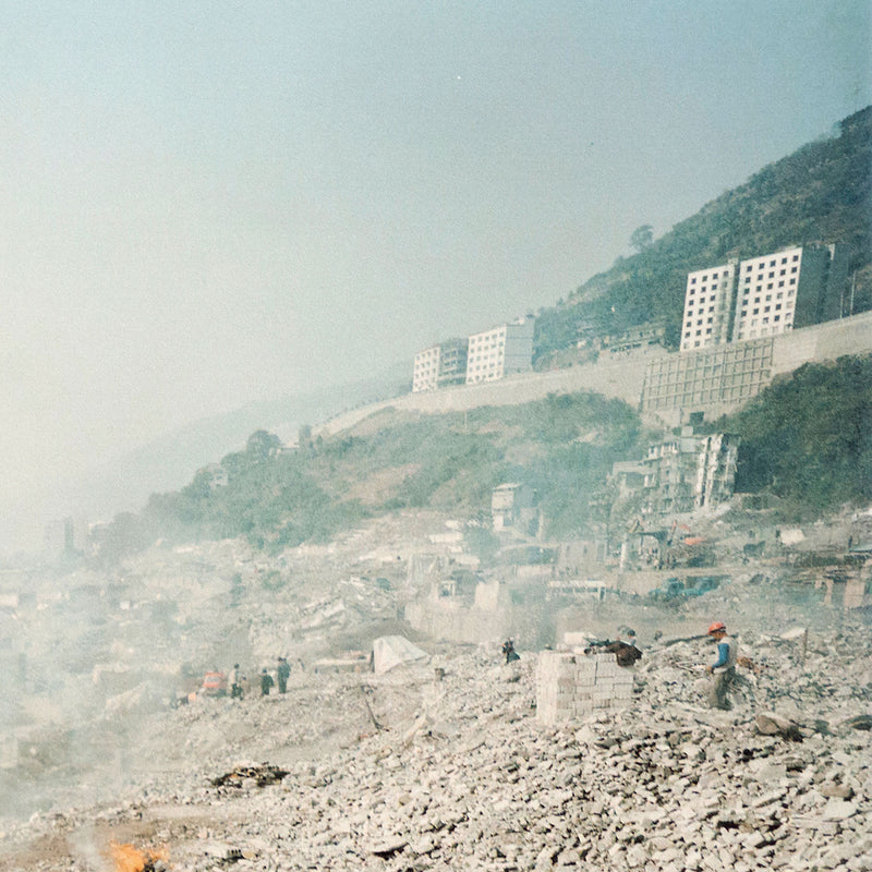 Shot in 2002, Canadian photographer Edward Burtynsky, captures "Feng Jie #5". Depicting a demolished landscape, the photograph is marked by piles of rubble and a dusty haze that obscures the background. Centered in the middle of the work is a man leading his donkey down a dirt road amidst the destruction.