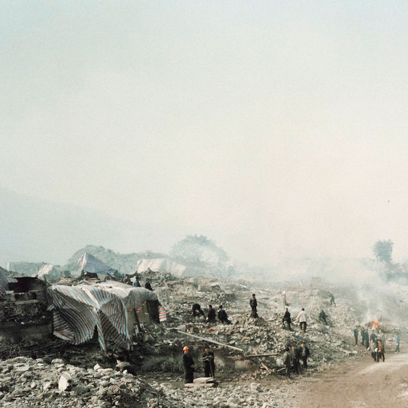 Shot in 2002, Canadian photographer Edward Burtynsky, captures "Feng Jie #5". Depicting a demolished landscape, the photograph is marked by piles of rubble and a dusty haze that obscures the background. Centered in the middle of the work is a man leading his donkey down a dirt road amidst the destruction.