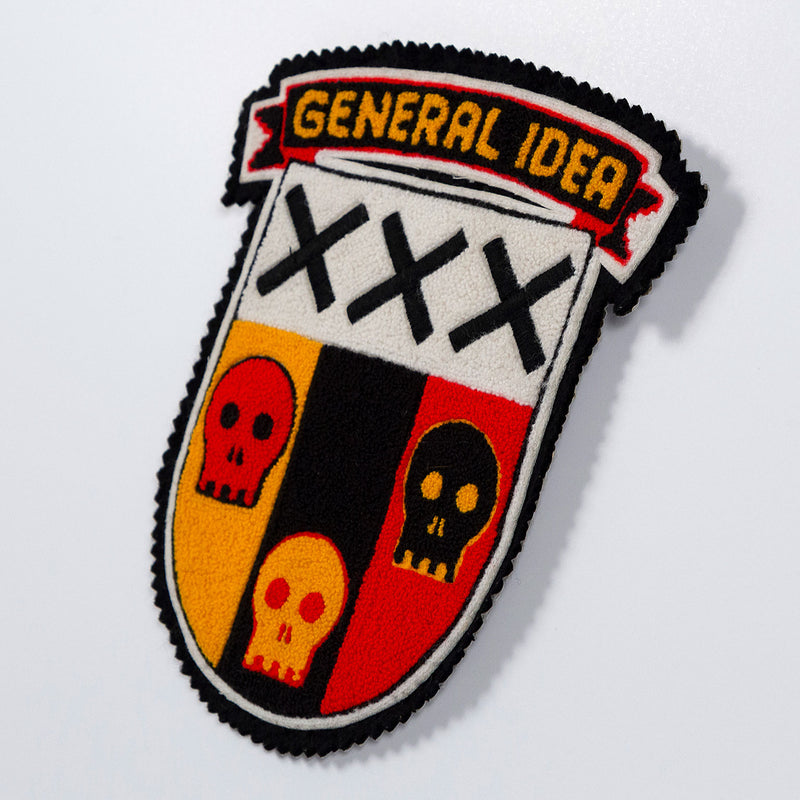 General Idea "Post Mortem" Chenille crest, 1988. Textile patch featurings a trio of skulls and alternating shades of yellow, red, and black.