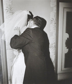 Diane Arbus "Groom Kissing his Bride" Gelatin silver print, 1966. Love and tension confront each other as the groom kisses the bride with an attacking passion. Her likeness disappears behind his embrace and their newlywed bodies merge together. This work also contains Arbus’ visual trademarks – a black and white palette, a square crop, and a hard flash that flattens the aesthetic wonderland of New York. 