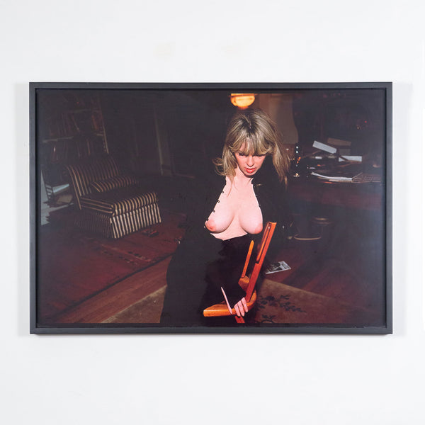 Nan Goldin "Joey with her New Breasts" Dye bleach print, 1999. Joey gently leans into the back of a chair, her chest bare and outwardly exposed. Joey's downward expression is partially hidden by her voluminous fringe, which contributes to her enigmatic presence and continuous glamour. 