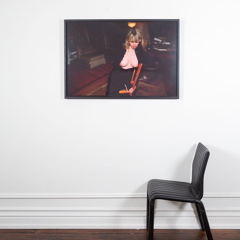 Nan Goldin "Joey with her New Breasts" Dye bleach print, 1999. Joey gently leans into the back of a chair, her chest bare and outwardly exposed. Joey's downward expression is partially hidden by her voluminous fringe, which contributes to her enigmatic presence and continuous glamour. 