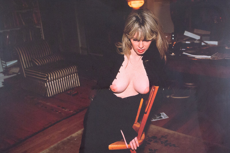 Nan Goldin "Joey with her New Breasts" Dye bleach print, 1999. Joey gently leans into the back of a chair, her chest bare and outwardly exposed. Joey's downward expression is partially hidden by her voluminous fringe, which contributes to her enigmatic presence and continuous glamour. 